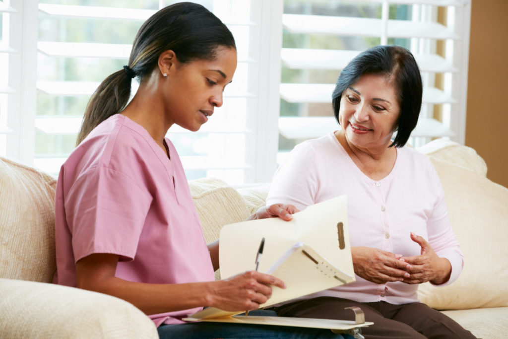 A nurse talking to a woman on a couch with paperwork