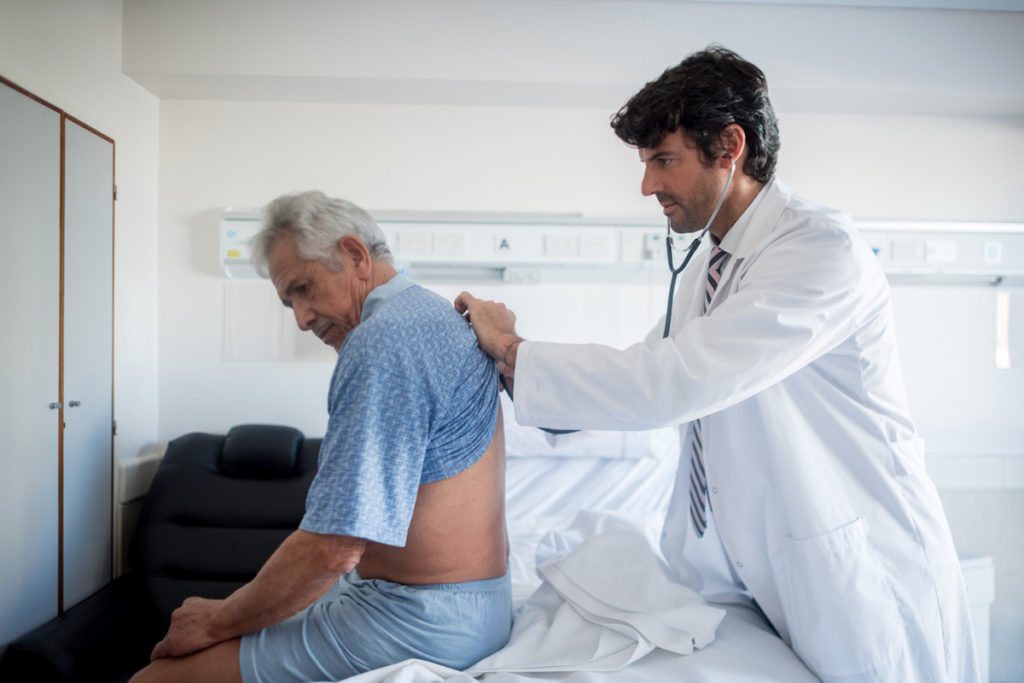 Doctor doing his medical rounds at the hospital listening to a senior patients lungs