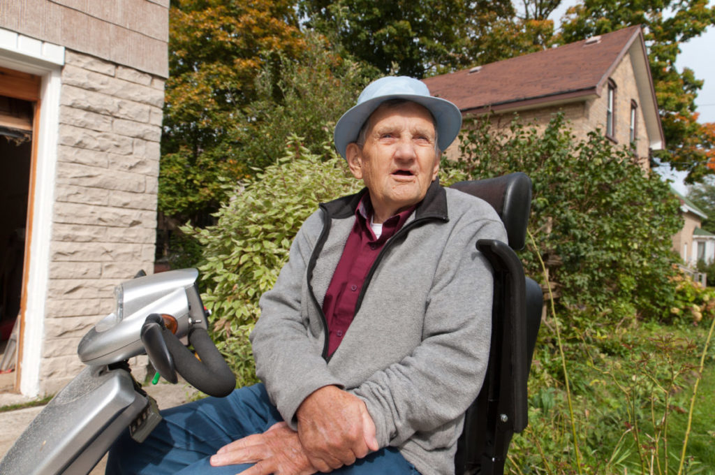 A late 70's senior male gazing forward while sitting on his electric scooter. Weather beaten face of a retired farmer.