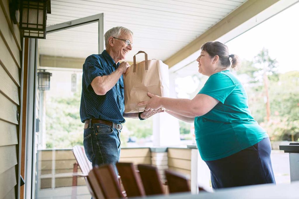 woman delivering groceries to a senior male