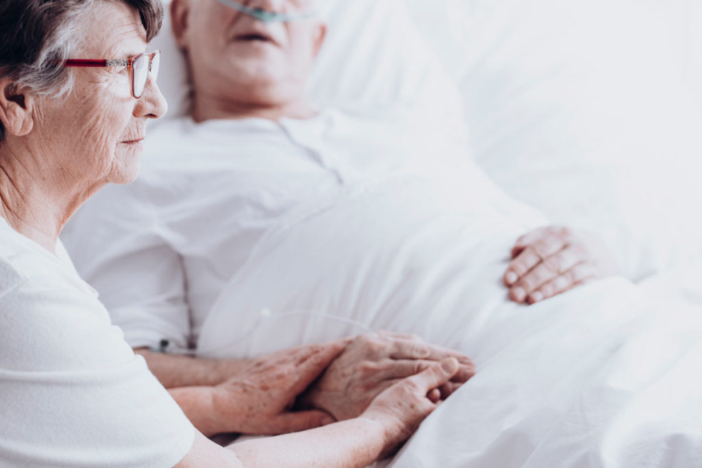 elderly man in hospital bed with wife holding hands