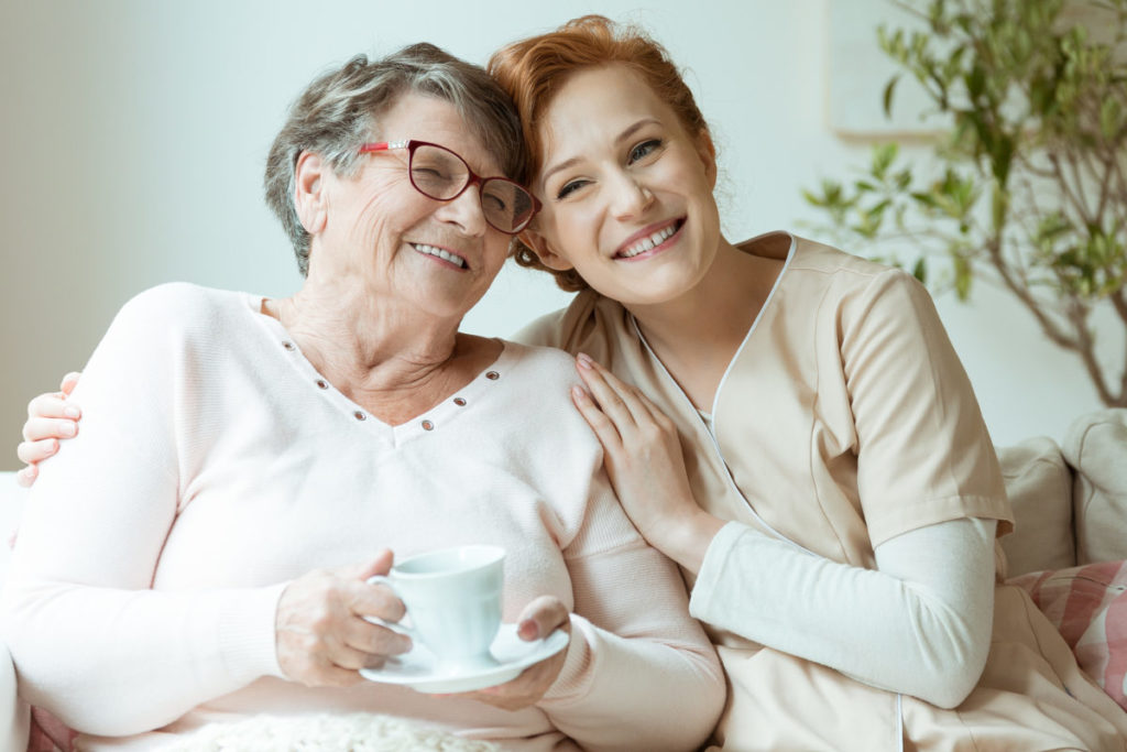 Smiling nurse in beige uniform hugs old lady