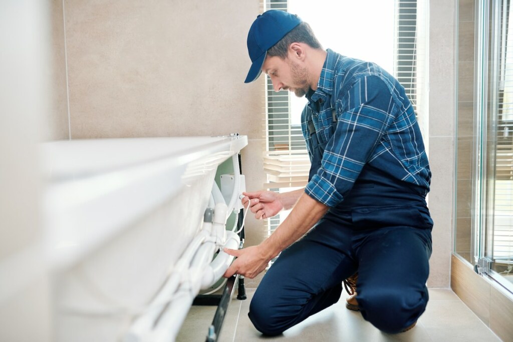 Contemporary technician installing pipe system by bathtub