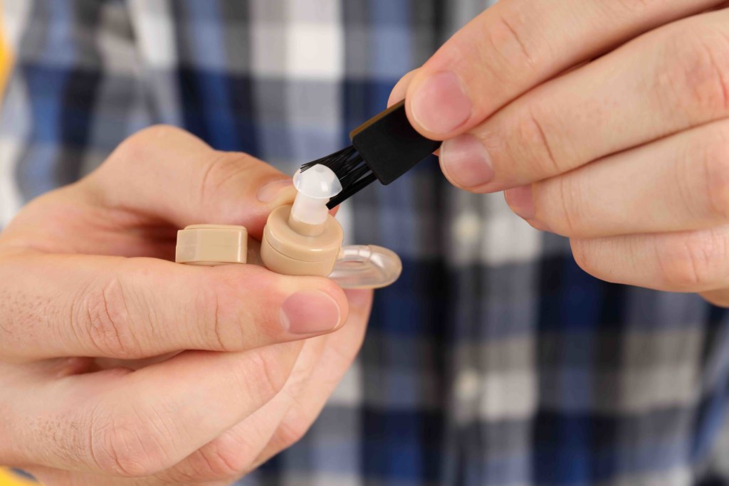 Young man cleans hearing aid, close up