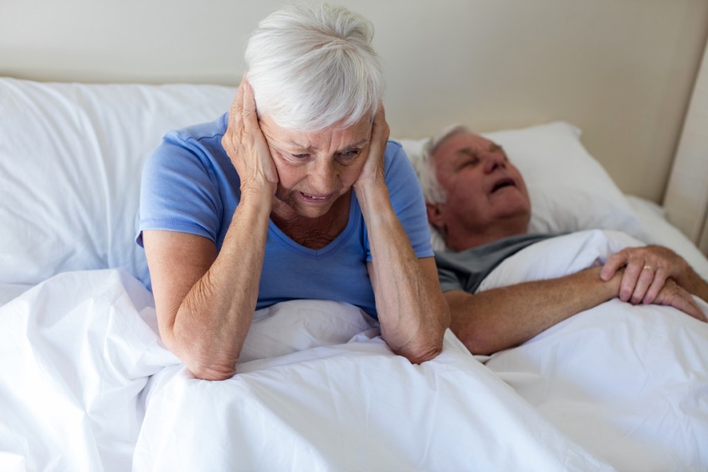 Senior woman getting disturbed with man snoring on a normal bed