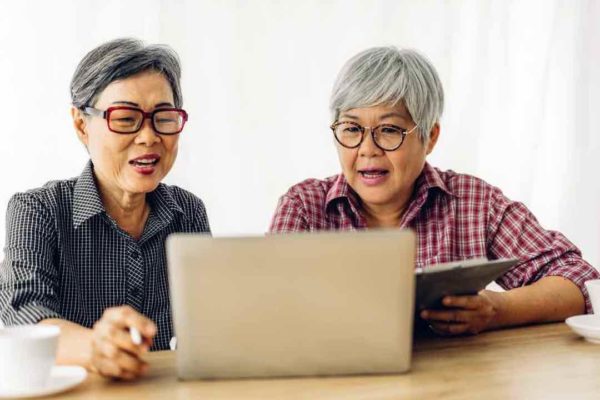 Portrait of two friend happy senior adult elderly asia women smiling and working with laptop computer at home. Retirement concept